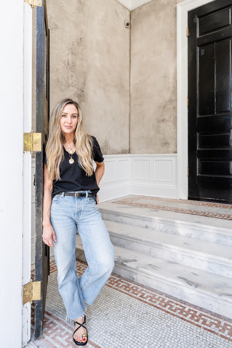 A picture of Emily Pope Harris standing in front of her entry vestibule plaster wall installation in downtown Charleston. Inside the vestibule the walls had a heavily textured layered plaster in dark grays, blacks, and browns. 