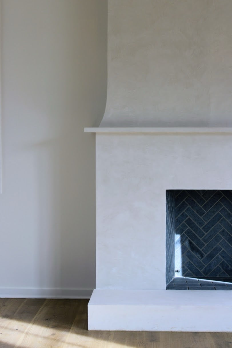 A detailed close up image of a two story plaster fireplace. It has a creamy Origami White venetian plaster finish with a burnish and a polish.  