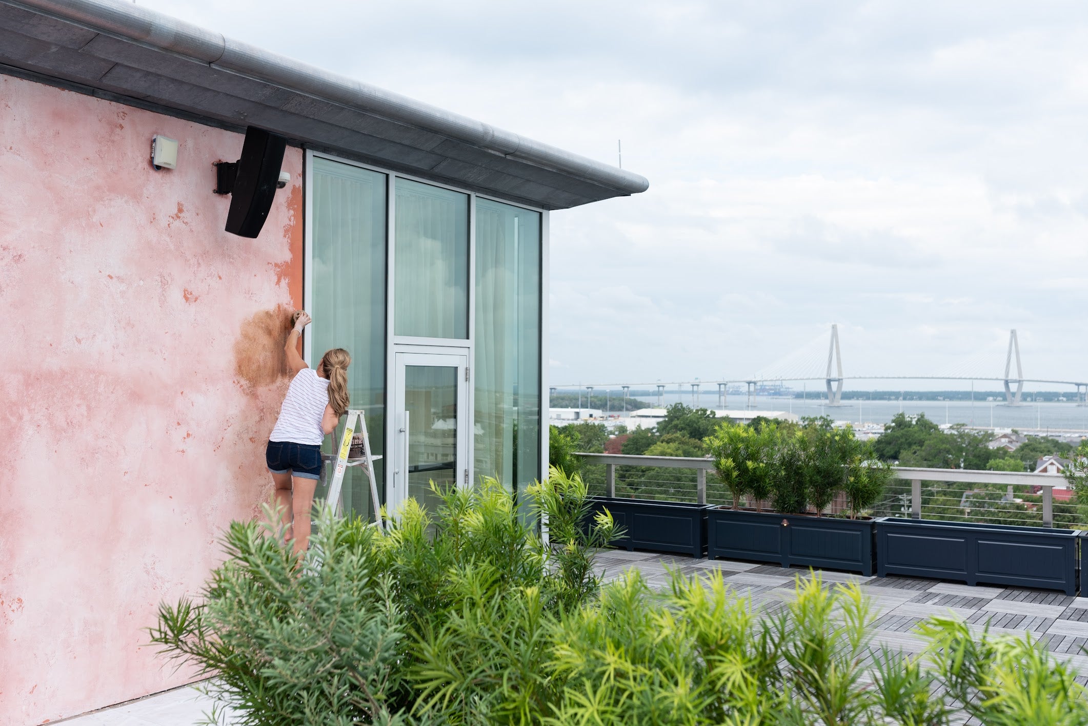 Emily glazing textured plaster at The Dewberry’s Citrus Club rooftop with Ravenel Bridge in the background.”