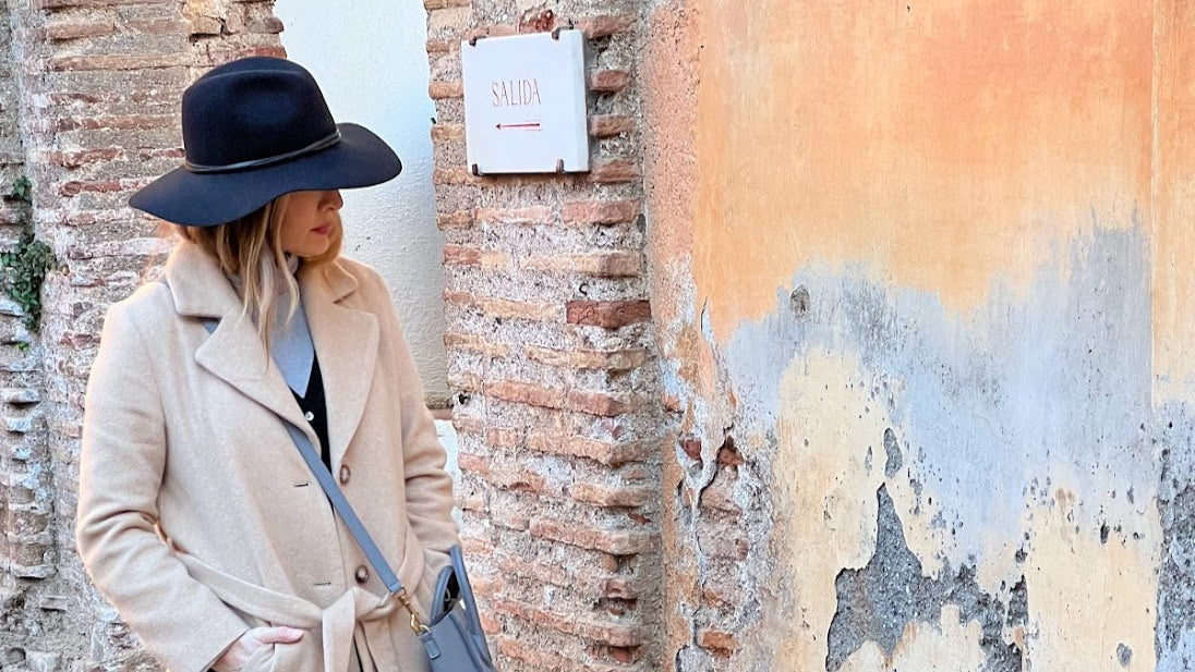 Emily Harris walking in front of a vibrant, layered historic plaster wall in Spain, drawing inspiration from the texture, color, and aged patina.