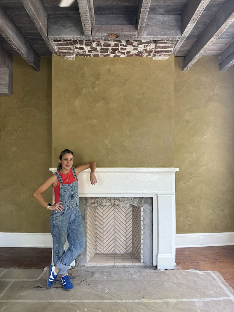 Emily Harris standing in front of her custom gold Venetian plaster fireplace in a historic downtown Charleston home.