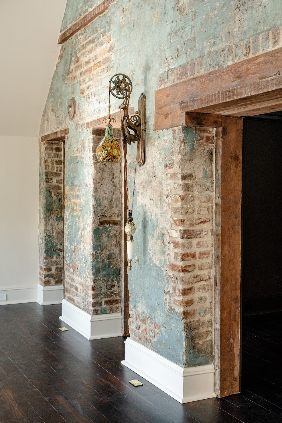 Historic Charleston living room brick wall with Emily’s layered plaster and glaze finish, revealing brick in spots for an aged, textured look.