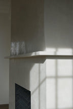 Side angle detail of a Venetian plaster fireplace mantle in a custom cream finish, showing the hand-burnished polish as light reflects across the surface at Kiawah River by Emily Pope Harris.