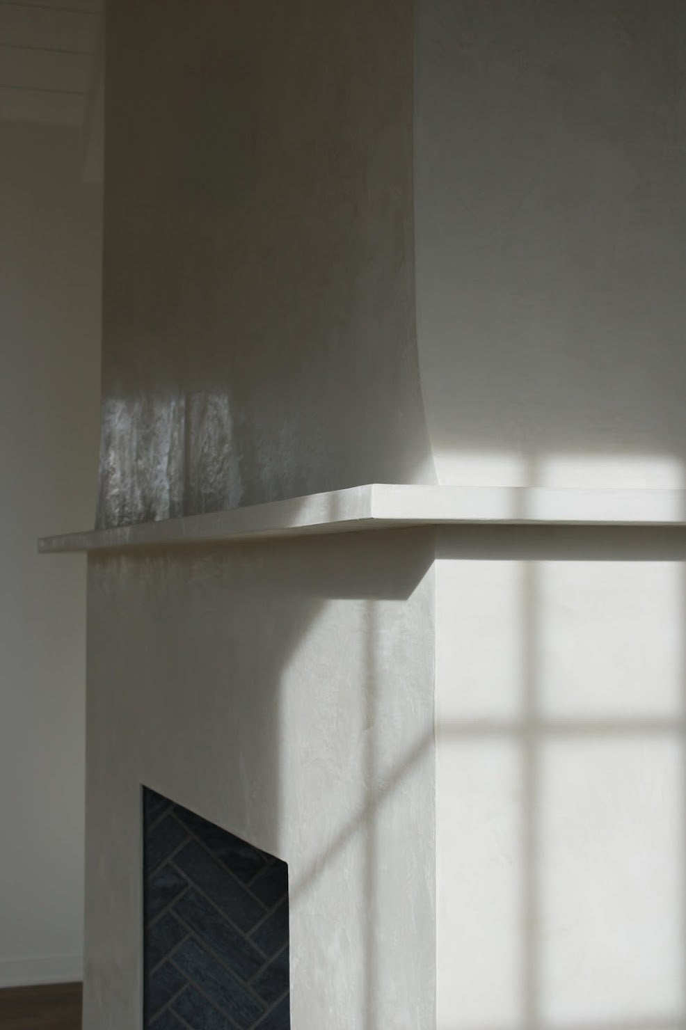 Side angle detail of a Venetian plaster fireplace mantle in a custom cream finish, showing the hand-burnished polish as light reflects across the surface at Kiawah River by Emily Pope Harris.