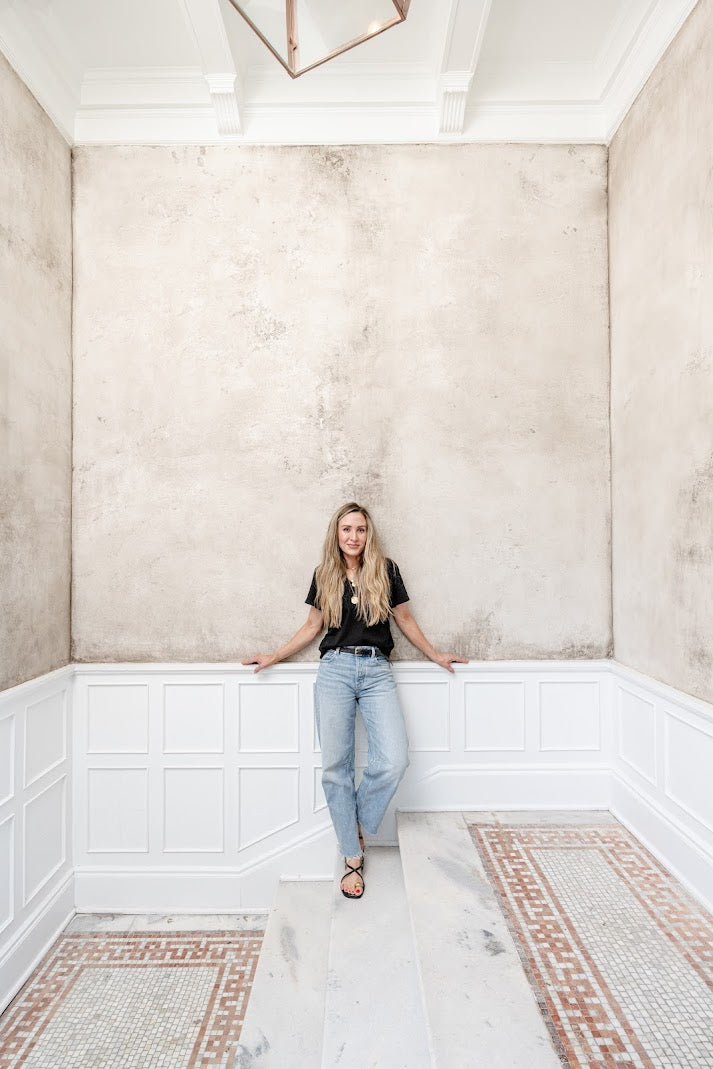 Emilys standing in front of the textured gray plaster entry vestibule in downtown Charleston with layered depth and movement, plaster installation by Emily Pope Harris, designed by Betsy Berry, featured in Charleston Home + Design magazine and photographed by Ruta Smith.