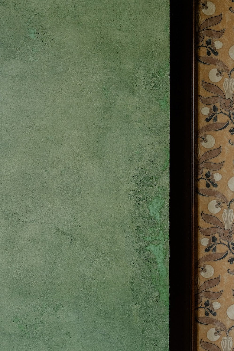 Detailed view of textured plaster wall with custom olive-green glaze beside bold patterned wallpaper and cabinetry at The Refinery in Charleston, SC by Emily Pope Harris.